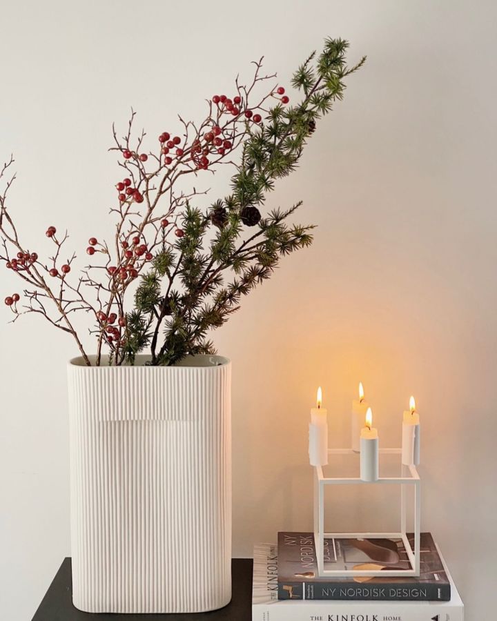 Unsere Geschenk-Ideen für Weihnachten: Hier sehen Sie die stilvolle Ridge Vase von Muuto mit Tannengrün darin und den weißen Kubus Kerzenhalter von Audo Copenhagen auf einem Stapel Bücher stehen.