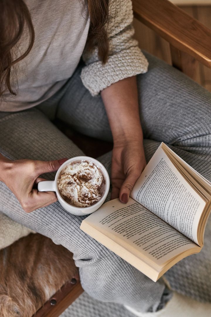 Jemand liest ein Buch und hält eine Tasse heißer Schokolade in der Hand.