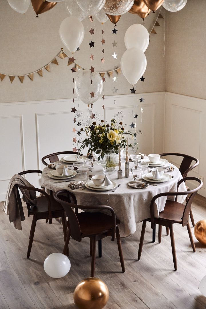 Ideen für Ihre Silvesterparty: Dekorieren Sie den Tisch mit von der Decke hängenden Ballons und Sternen in Weiß und Gold.