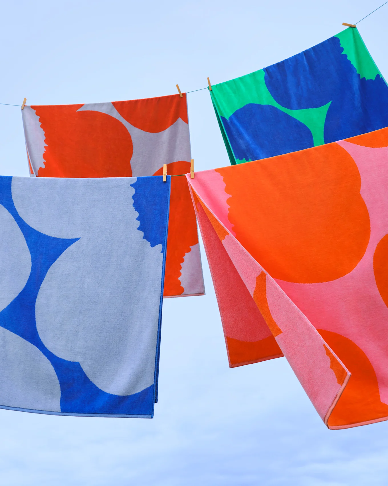 Bunt gemusterte Handtücher hängen an einer Wäscheleine vor blauem Himmel.