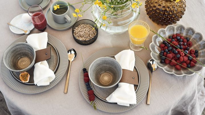Ein luxuriöser und gemütlicher Frühstückstisch für das Hotelfrühstück zu Hause mit Schalen von Mateus und Tellern von Eva Solo mit Saft und Beeren auf dem Tisch. 