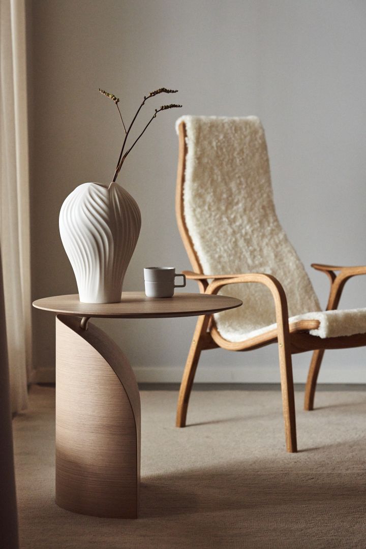 Swedese – die Marke hinter dem Lamino-Sessel: Hier sehen Sie den Savoa Tisch und den Lamino Sessel mit weißem Schaffell und Eichenholz der schwedischen Möbelmarke Swedese.
