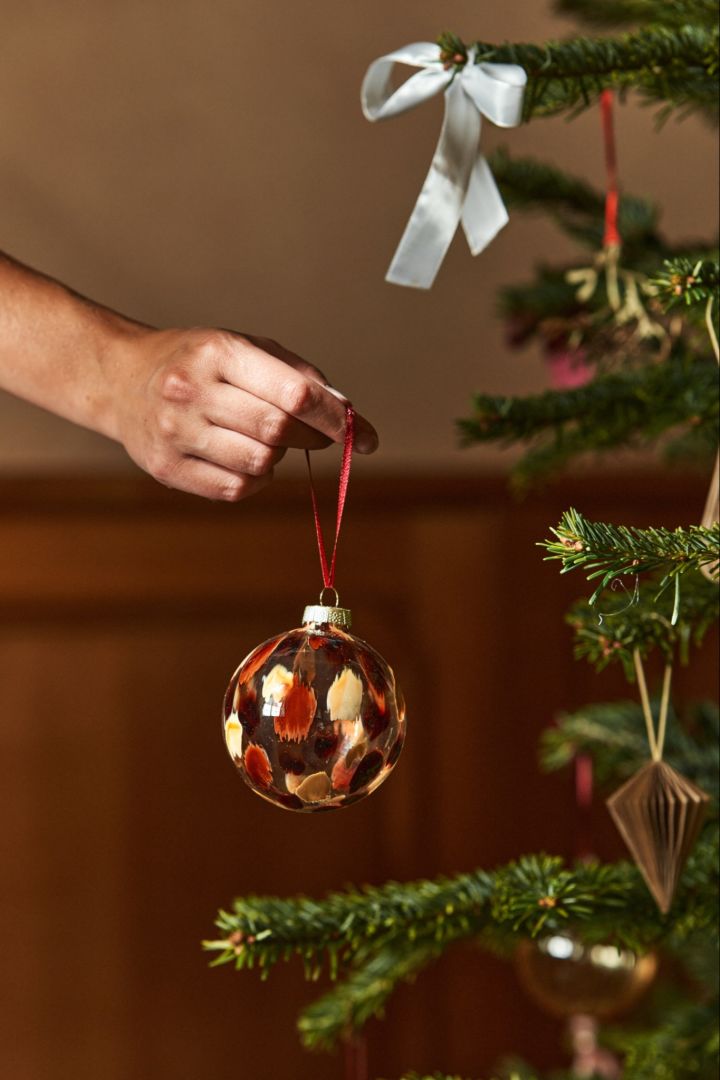 Eine Hand hält eine Glaskugel in einem Baum. Glasdekorationen sind für Weihnachten 2024 so beliebt wie eh und je. 