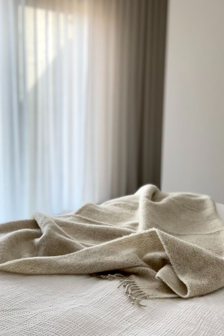 Eine klassische Wolldecke, wie beispielsweise die Sandstone Wolldecke in Beige von Scandi Living, welche hier auf einem Bett liegt, ist stets eine gute Geschenkidee zur Hochzeit.
