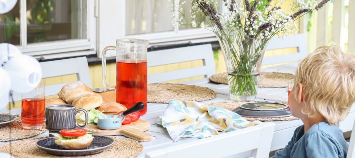 Das Bild zeigt einen kleinen Jungen, der an einem Frühstückstisch mit frisch gebackenen Brötchen sitzt.