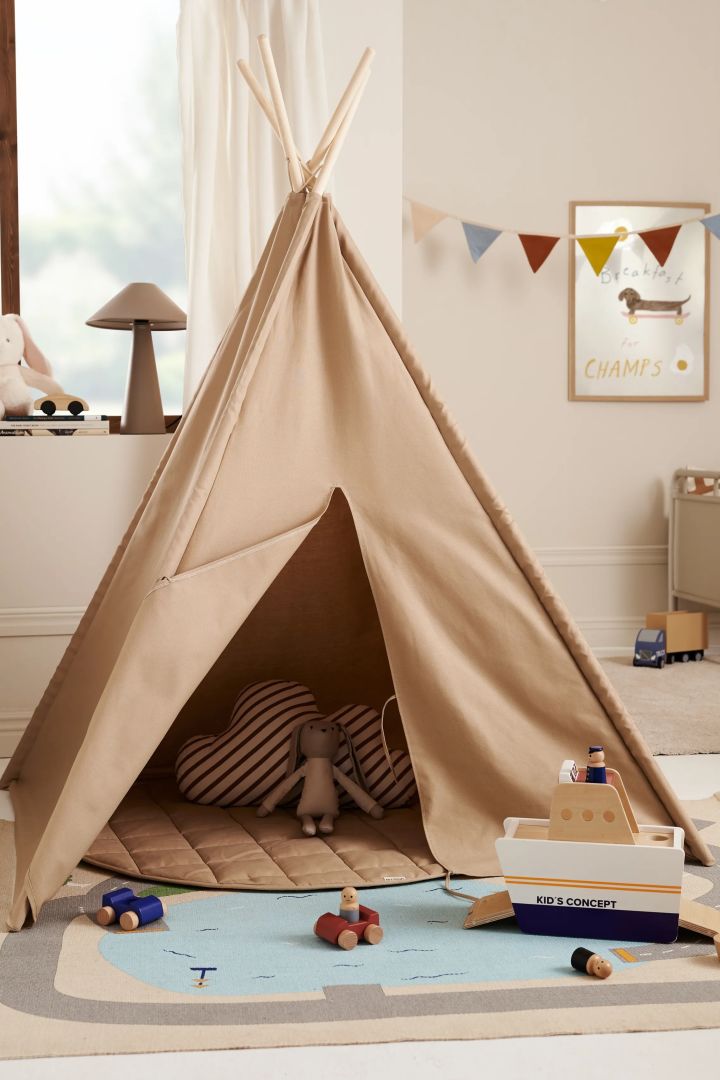 Ein Tipi-Zelt eignet sich hervorragend für ein Kinderzimmer, in dem es sich Ihr Kind mit einem Buch gemütlich machen kann. Hier sehen Sie ein Tipi-Zelt in Beige in einem Kinderzimmer. 