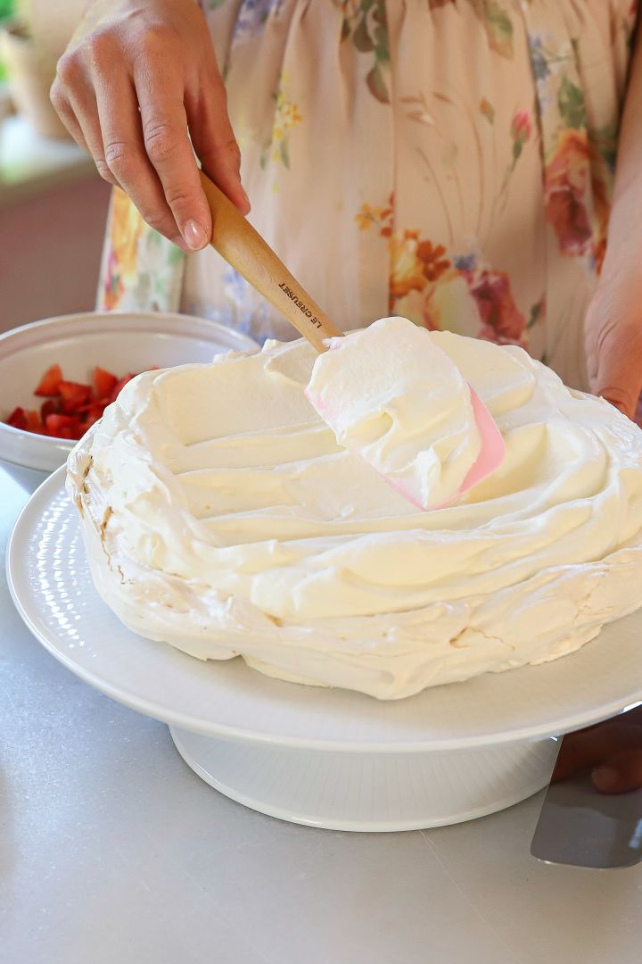 Die schwedische Back-Influencerin Baka med Frida verrät Ihnen ihre einfachen Tortenrezepte zu Mittsommer, beispielsweise eine knusprige Baisertorte mit Sahne, welche sie hier mit einem Spatel von Le Creuset auf der Baiser-Masse verteilt.