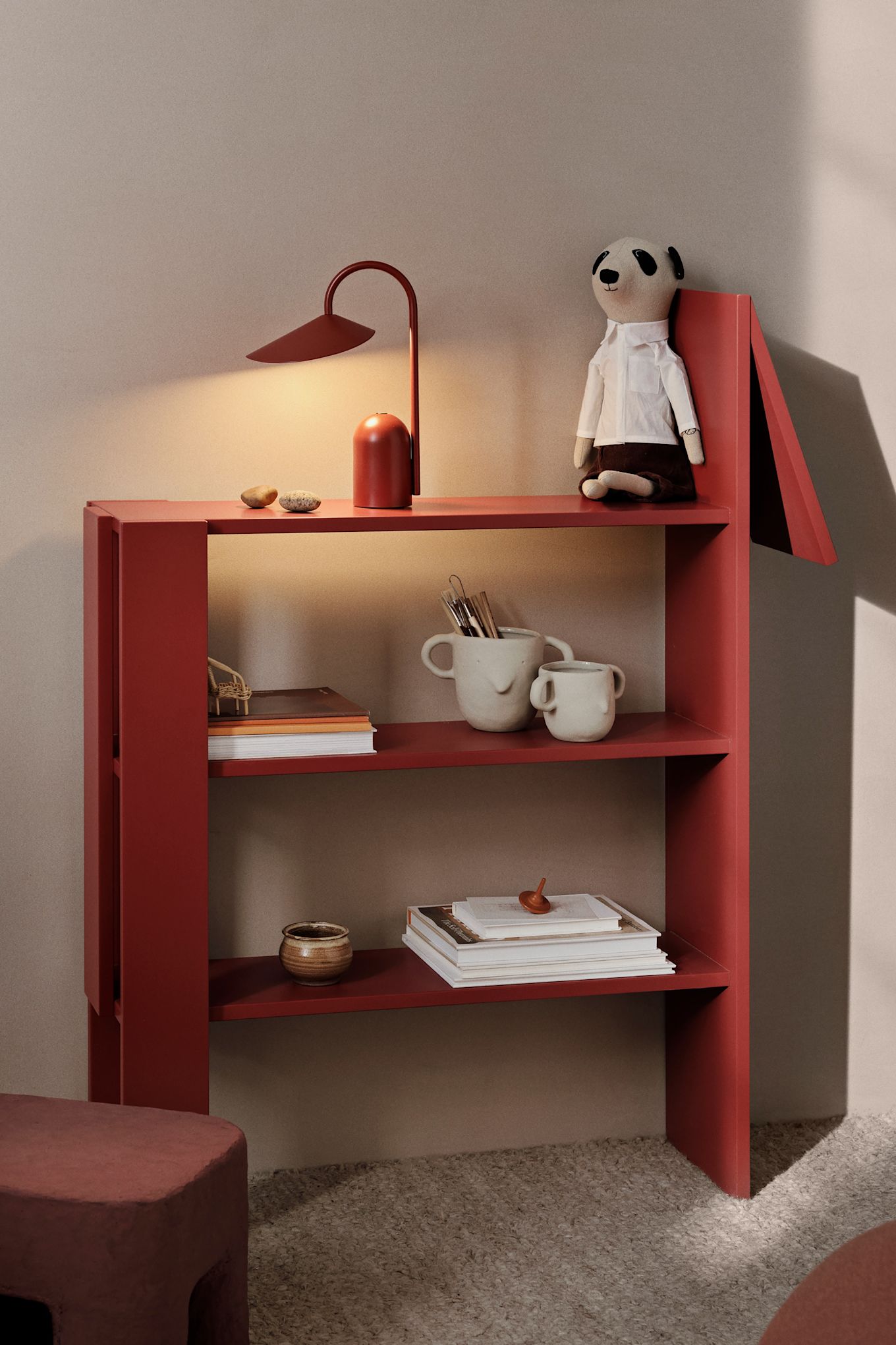 Farbe ins Kinderzimmer zu bringen ist eine tolle Idee. Hier sehen Sie das Giraffenregal von Ferm Living in einem knalligen Rot, dekoriert mit einer roten tragbaren Lampe und einigen Kuscheltieren. 