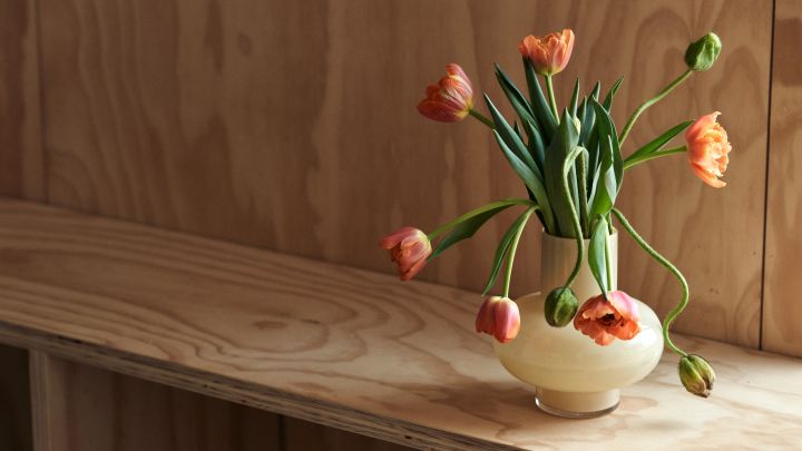 Wir hier bei Nordic Nest möchten Ihnen Tipps für die Einrichtung Ihres Zuhauses und die neuesten Einrichtungstrends näherbringen. Hier sehen Sie eine gelbe Vase von Marimekko mit orangefarbenen Tulpen darin. 