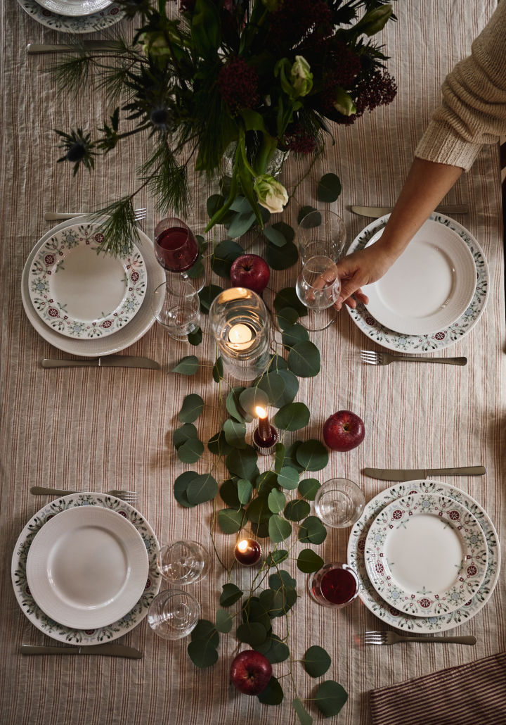 Ein weihnachtlich gedeckter Tisch, von oben fotografiert, mit grünen Blättern und roten Äpfeln als Dekoration. 