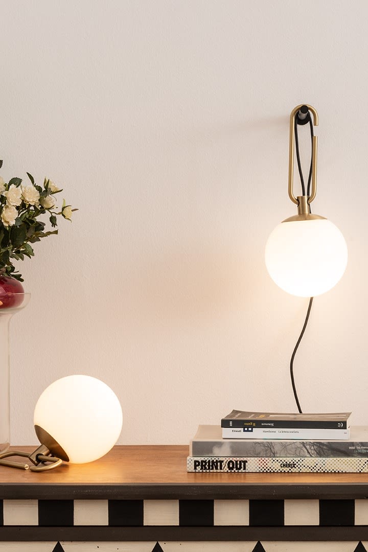 Die NH Wand- und Tischleuchten von Artemide hängen und stehen auf einem Schreibtisch mit einem Stapel Bücher.