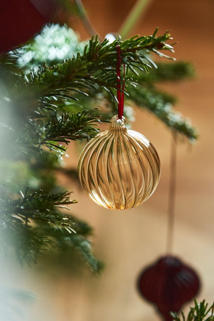 Hier sehen Sie die goldene Clarity-Kugel von Scandi Living, die in einem Baum hängt. Glasdekorationen sind auch im Jahr 2024 beliebt wie eh und je. 