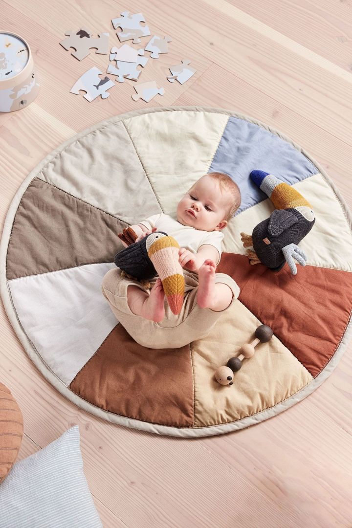 Das Trine Tourca Plüschtier von OYOY liegt neben einem Baby auf dem Moni Kinderteppich. Das Plüschtier besteht ausschließlich aus recycelten Materialien und macht es damit nicht nur zu einem tollen, sondern auch zu einem nachhaltigen Geschenk zur Babyparty.