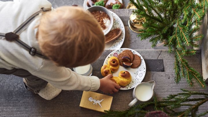 Hier sehen Sie ein Kind, das nach einem Lussekatt greift, das auf einem Teller aus der Swedish Grace Winter-Kollektion von Rörstrand liegt.