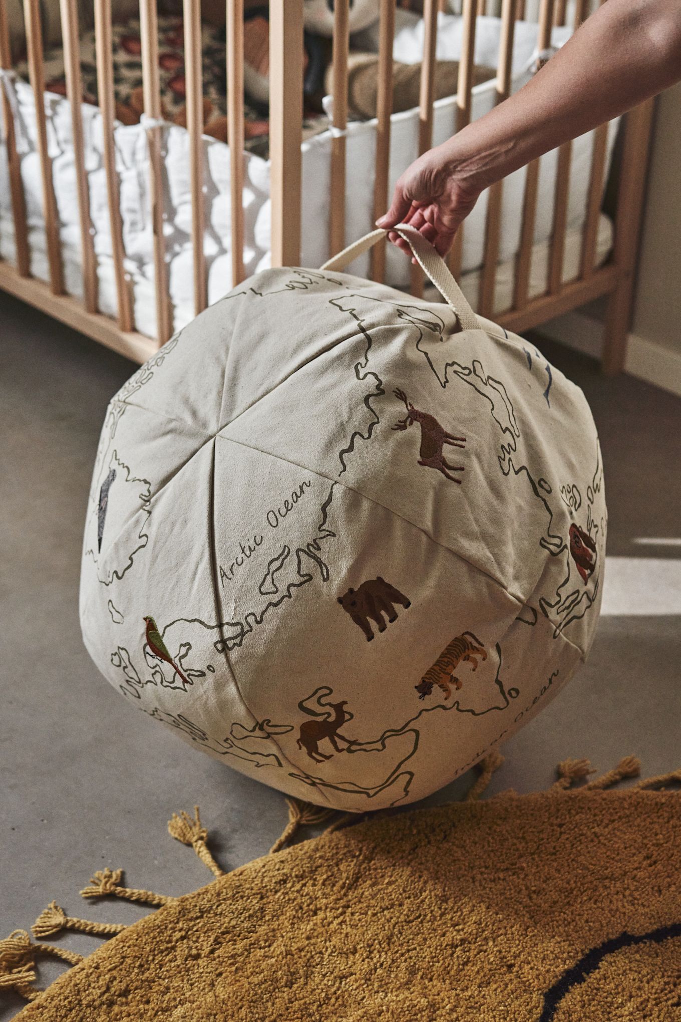 Eine Weltkarte und ein Sitzsack in einem - hier sehen Sie eine Hand, die den World Pouf von Ferm Living hält, eine tolle Idee für ein Kinderzimmer. 