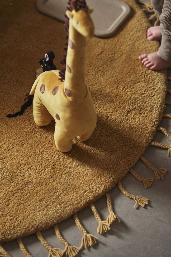 Es ist eine tolle Idee, mit Kuscheltieren und anderen Accessoires Farbe in ein Kinderzimmer zu bringen. Hier sehen Sie eine Giraffe von Bloomingville auf dem Sonnenteppich von ferm LIVING. 