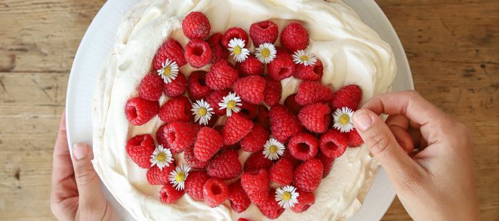 Eine leckere Baisertorte ist eines der einfachen Tortenrezepte von Baka med Frida. Dekorieren Sie die weiße Torte aus Baiser und Sahne mit frischen roten Himbeeren und hübschen Gänseblümchen.