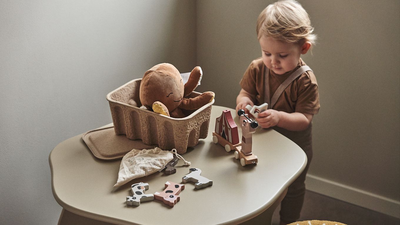 Ein Kind spielt mit Holzspielzeug, das aus einer Aufbewahrungsbox aus Papier stammt – eine praktische Idee für das Kinderzimmer. 