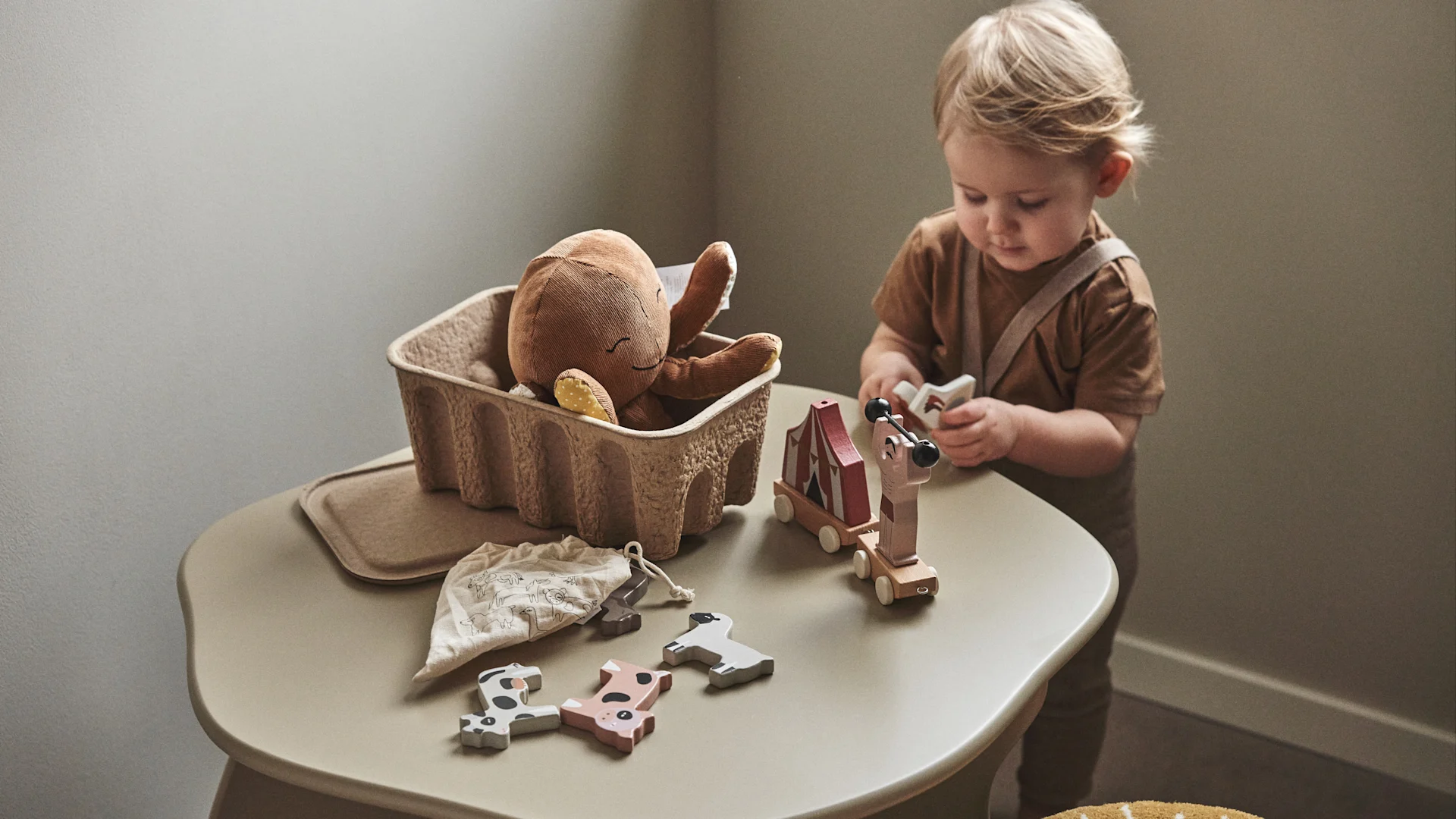 Ein Kind spielt mit Holzspielzeug, das aus einer Aufbewahrungsbox aus Papier stammt – eine praktische Idee für das Kinderzimmer.