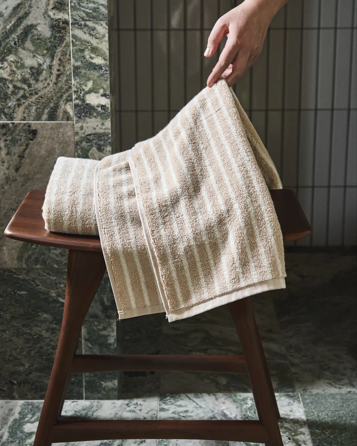 Hand legt ein beige-weiß gestreiftes Handtuch auf einen Holzschemel.