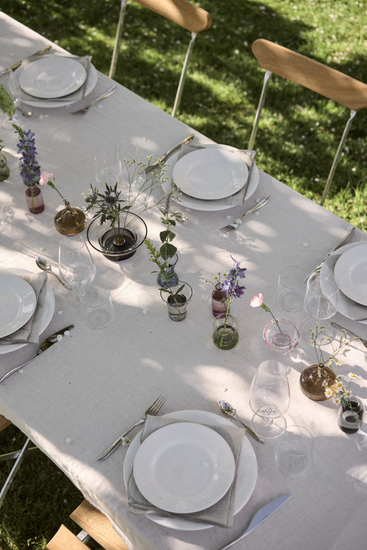 Hier sehen Sie einen in Weiß gedeckten Tisch zu Mittsommer in Schweden, auf welchem die Midsummer-Vasen von Orrefors als Blickfang in der Mitte angeordnet sind.