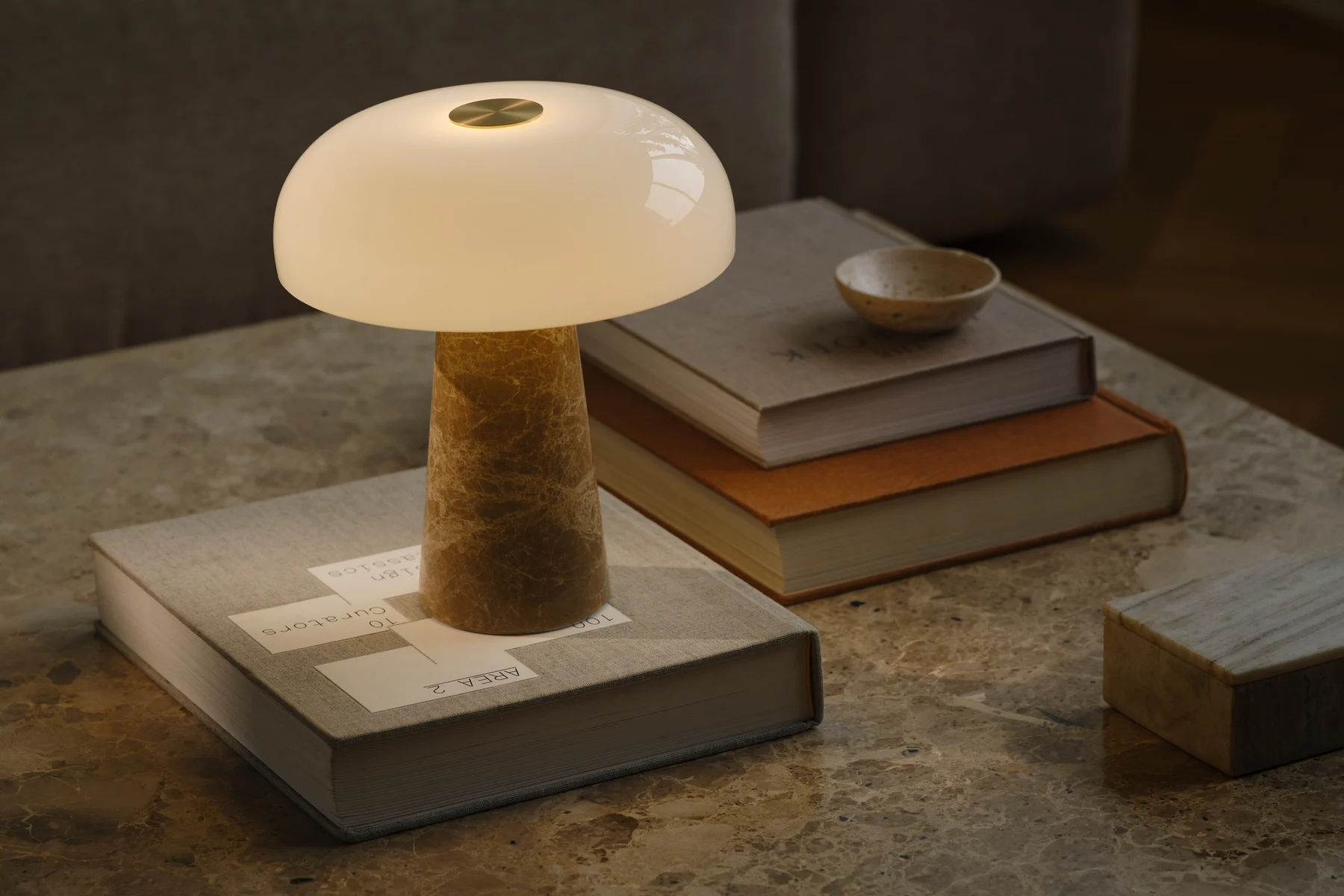Eine pilzförmige Tischlampe mit weißem Glasschirm und konischem Marmorsockel steht auf einem Marmortisch mit gestapelten Büchern.