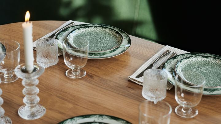 Entwerfen Sie klassisches Ostindia-Blumengeschirr in Grün für einen gedeckten Tisch im Restaurantstil mit klobigen Kerzenhaltern aus Glas. 