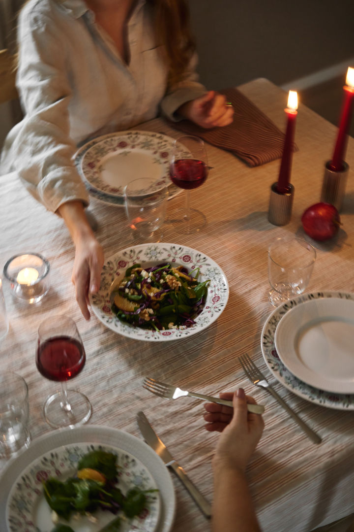 Eine Hand reicht einen Wintersalat über den weihnachtlich gedeckten Tisch.