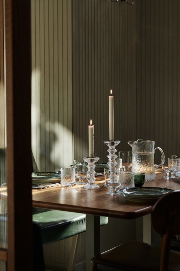 Hier sehen Sie einen grün gedeckten Tisch in einer Restaurantumgebung mit klobigen Kerzenhaltern aus Glas und einem passenden Wasserkrug. 