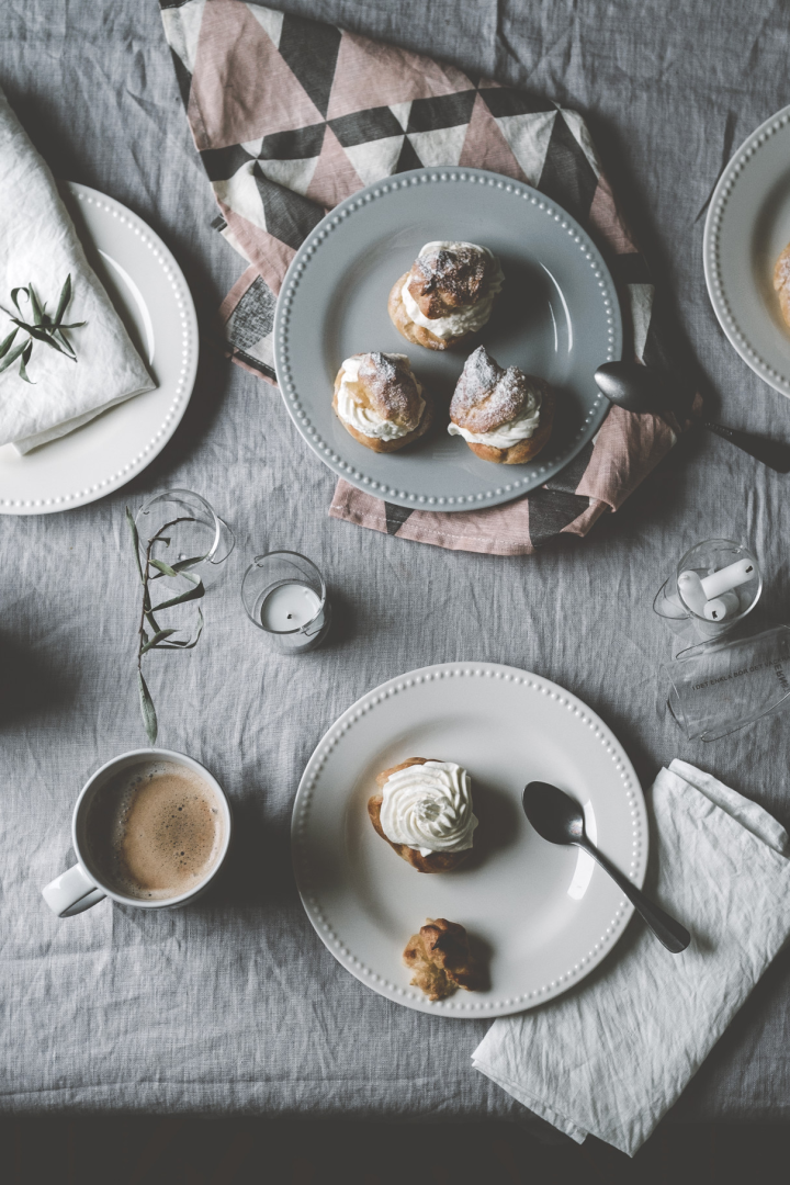 Hier sehen Sie die Semlor von @kohlundkimchi auf verschiedenfarbigen Tellern aus der Dots-Kollektion von Scandi Living auf einem Tisch stehen, dazu eine Tasse Kaffee.