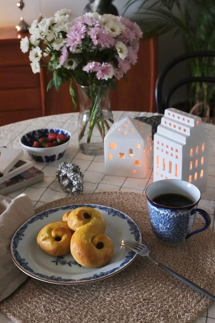 Hier sehen Sie einen Tisch mit frischen Blumen und weihnachtlicher Dekoration in Form von Urbania Kerzenleuchtern von Kähler und schwedischen Lussekatter auf einem Ostindia-Teller von Rörstrand im Zuhause von @_mariano_rivera_4242.