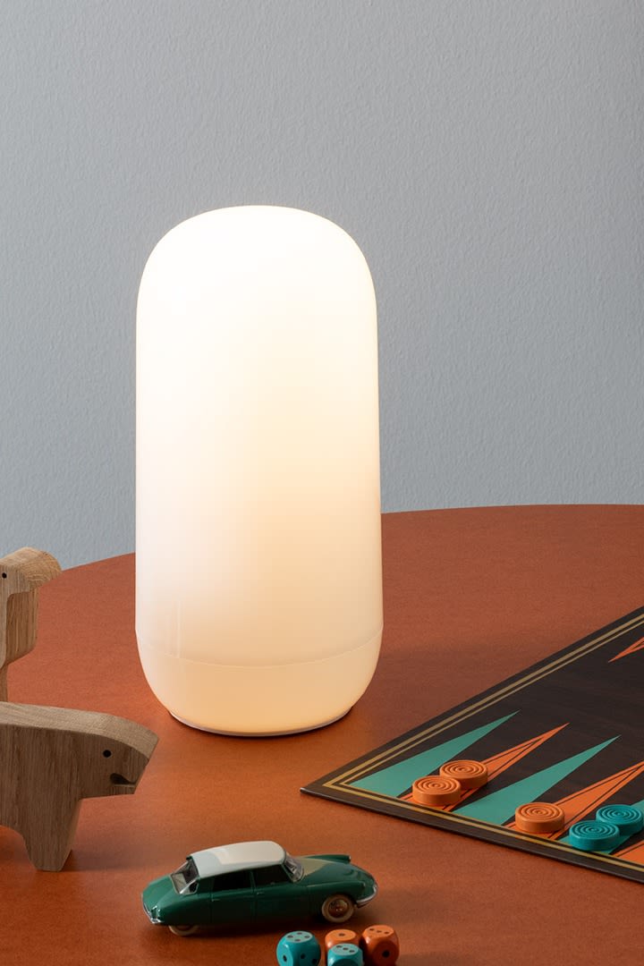 Die tragbare Lampe Gople von Artemide steht auf einem Schreibtisch mit Holzspielzeug und einem Backgammon-Spiel. 